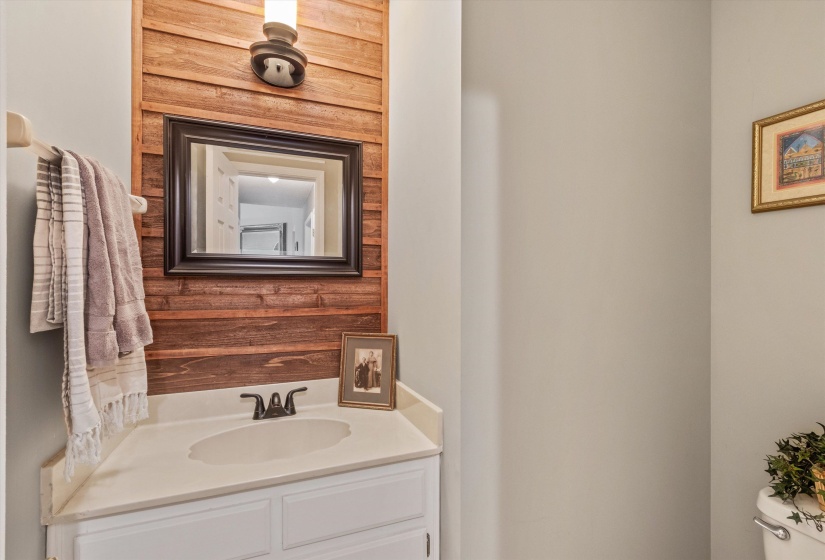 Vanity featuring a wood-finish accent wall, sconce lighting, and a framed mirror