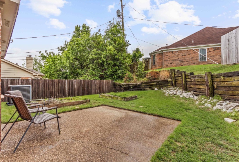 Expansive backyard featuring a concrete patio, a tiered retaining wall, a wood plank fence, and a manicured lawn