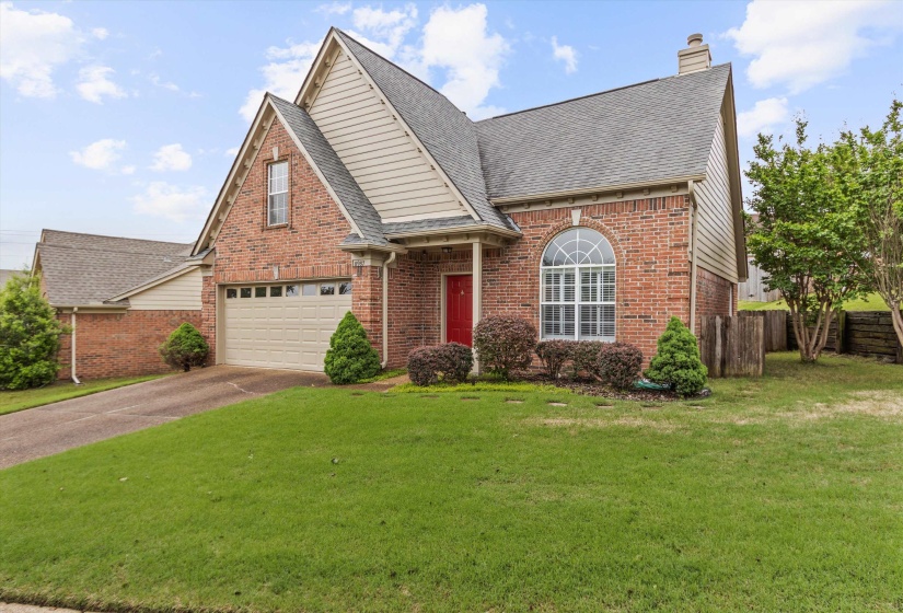 Brick exterior with a prominent arched window, a red entry door, and a light-toned garage door