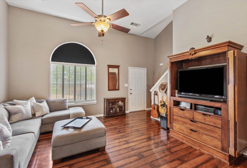 Living area featuring wood-finish flooring, vaulted ceilings, and a ceiling fan with light fixture