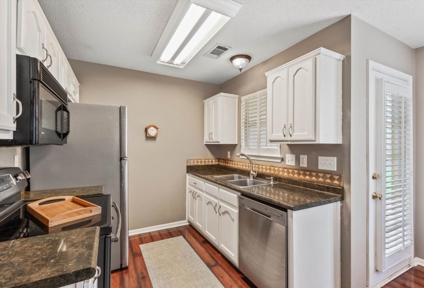 Kitchen featuring white cabinetry, dark stone-finish countertops, stainless steel appliances, and wood-finish flooring