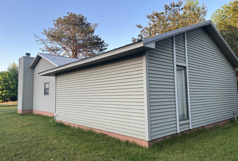 Contemporary exterior featuring light gray horizontal siding, a prominent metal roof, a full-height window with vertical trim, and a matching chimney structure