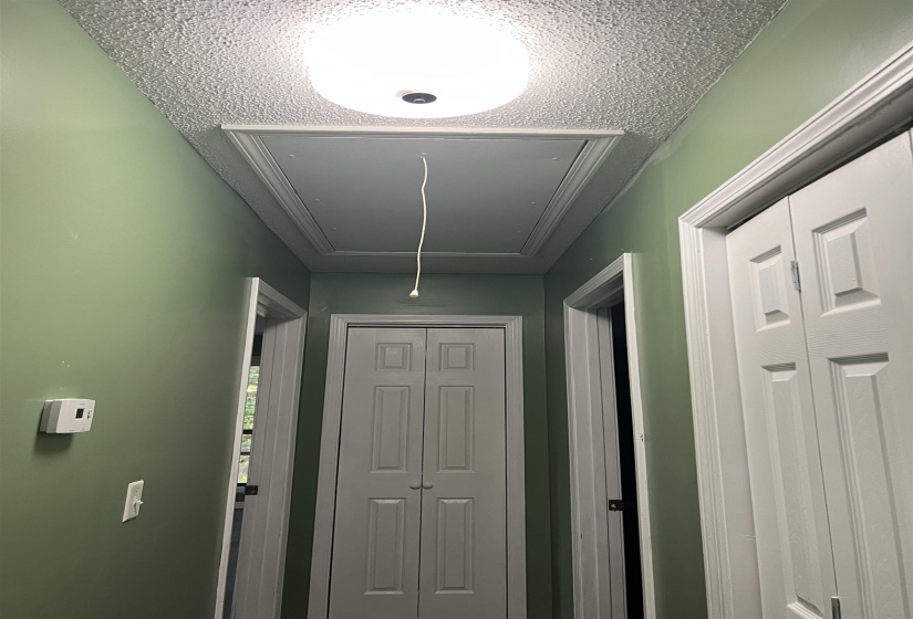 Hallway with light green walls, white trim, and a textured ceiling