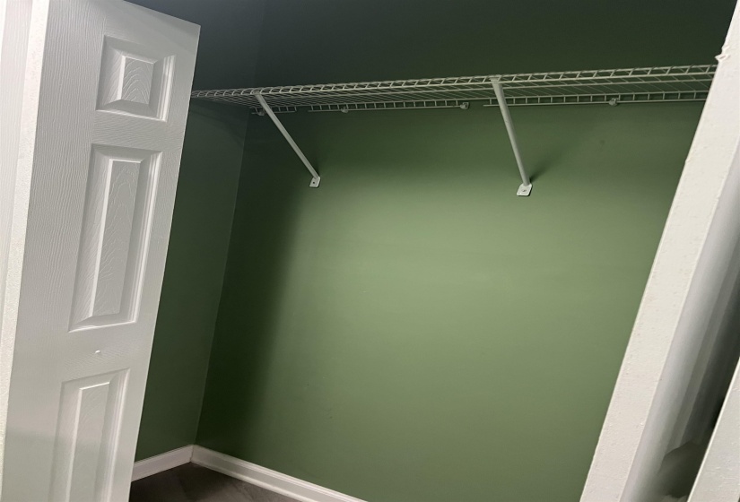 Closet interior featuring a wire shelving system, verdant wall color, white bi-fold doors, white baseboards, and wood-finish flooring