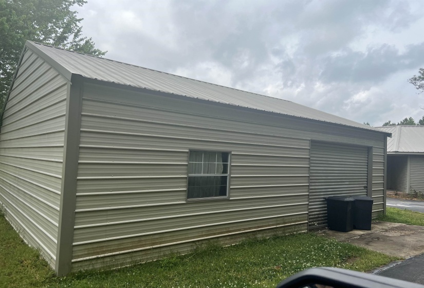 Metal-sided outbuilding featuring a roll-up door, single window, and a pitched metal roof and side walk in door