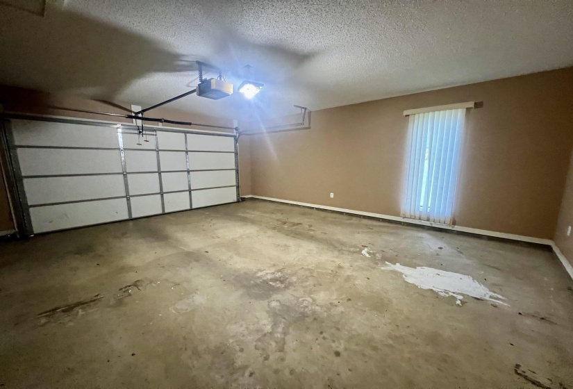 Spacious garage featuring a paneled overhead door, an automatic opener, a window with vertical blinds, and concrete flooring