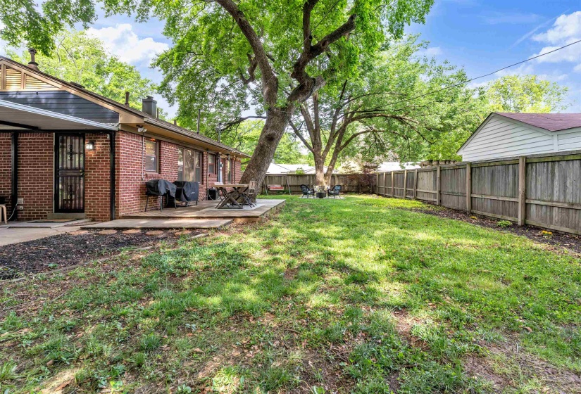 Expansive lawn area featuring a mature tree, wood fencing, and a concrete patio