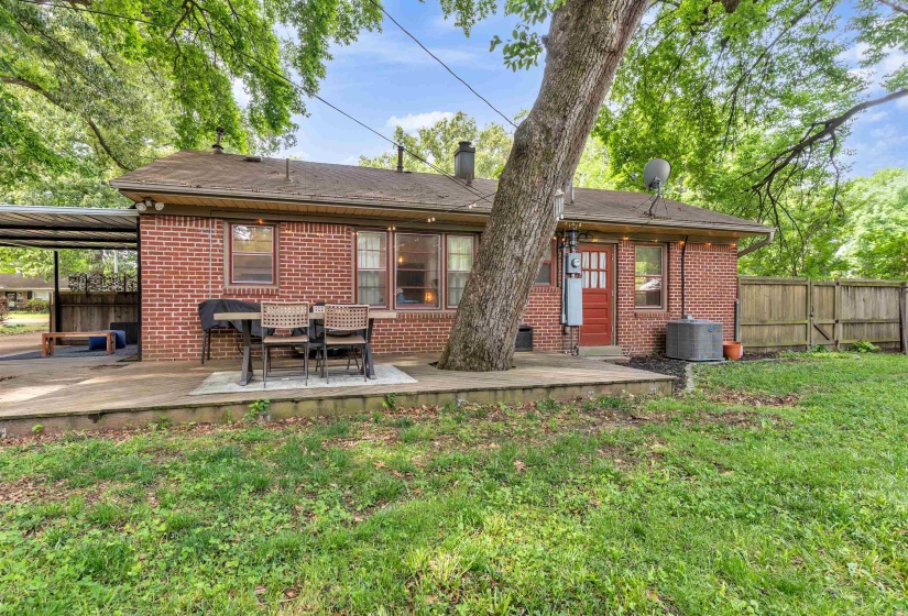 Rear brick exterior featuring a covered patio, additional concrete patio, fenced backyard, and mature trees