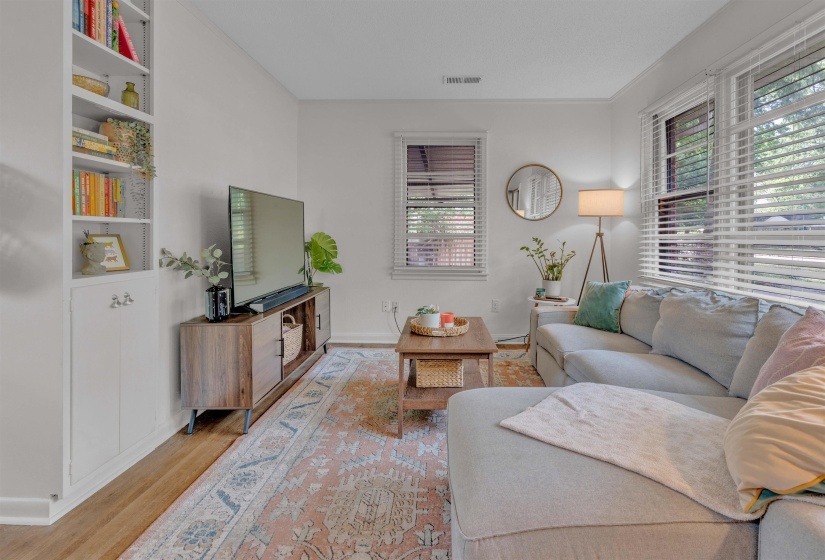 Living area featuring multiple windows with blinds, wood-finish flooring, and built-in white shelving