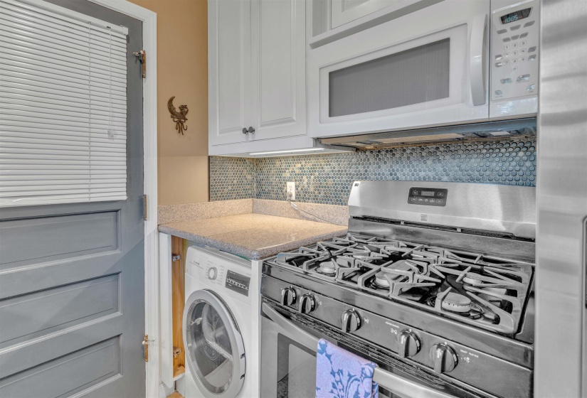 Compact kitchen featuring a stainless steel gas range, over-the-range microwave, white cabinetry, and a penny tile backsplash