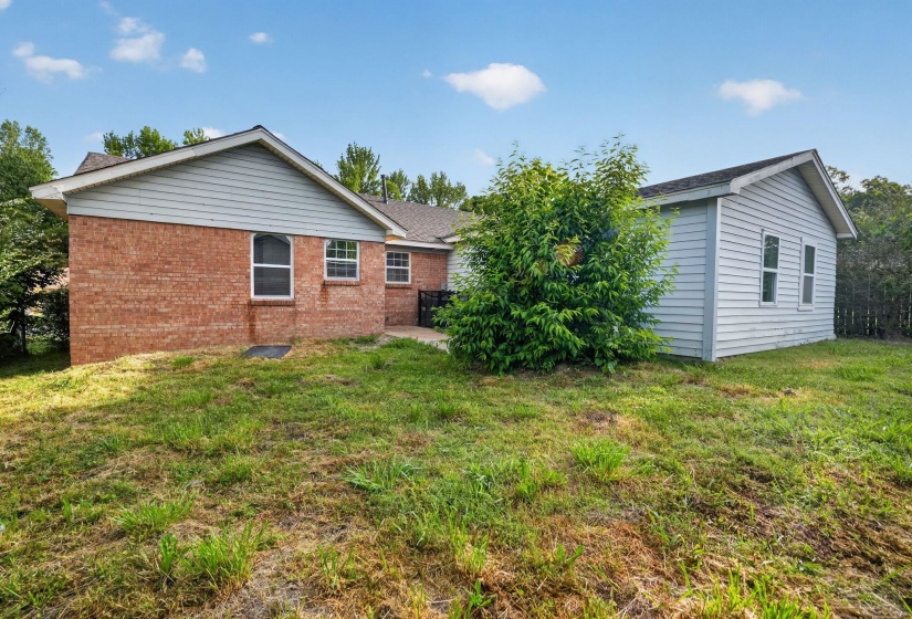 Expansive rear yard featuring a brick-sided residence with multiple windows, an additional detached structure with horizontal siding, and mature landscaping