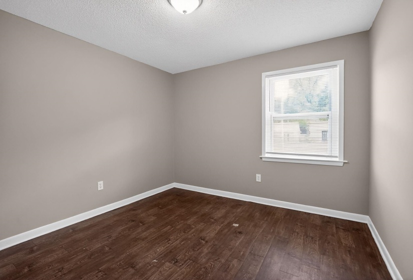 Room featuring wood-finish flooring, a neutral wall palette, white baseboards, a single window with blinds, and a ceiling-mounted light fixture