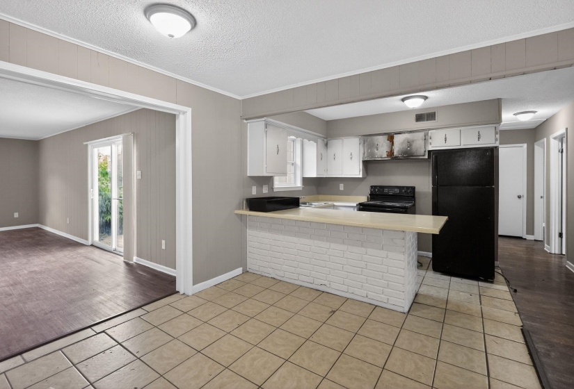 Kitchen featuring white cabinetry, black appliances, a white brick-look island, and tile flooring