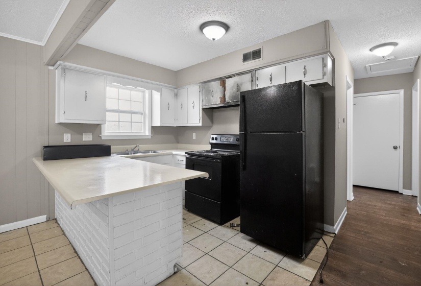 Kitchen featuring a white brick peninsula with a light-toned countertop, white cabinetry, a double-basin sink, and tile flooring