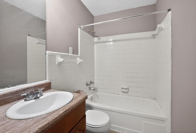 Bathroom featuring a vanity with an integrated sink, a large wall-mounted mirror, a bathtub with a shower, and white tile surround