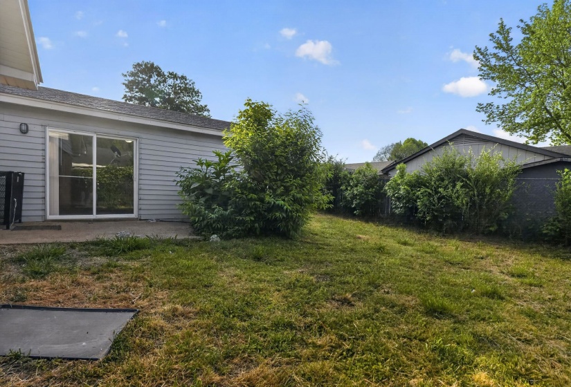 Expansive grassy backyard featuring a concrete patio, sliding glass door entry, and mature perimeter landscaping