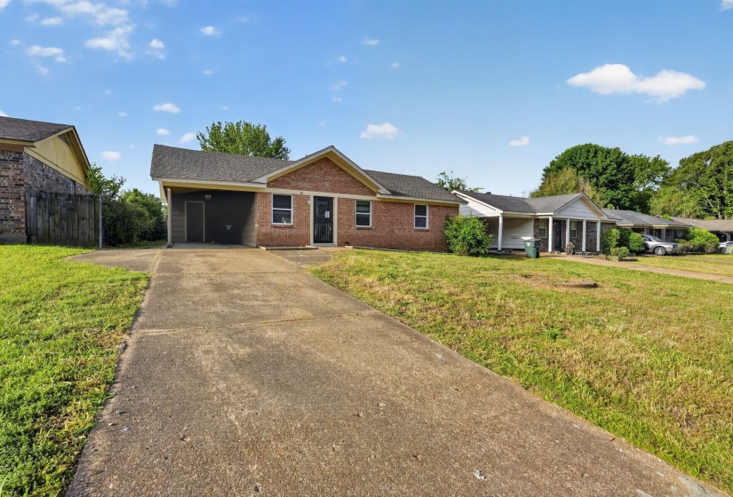 Brick facade residence featuring a covered carport, a concrete driveway, and a fenced side yard