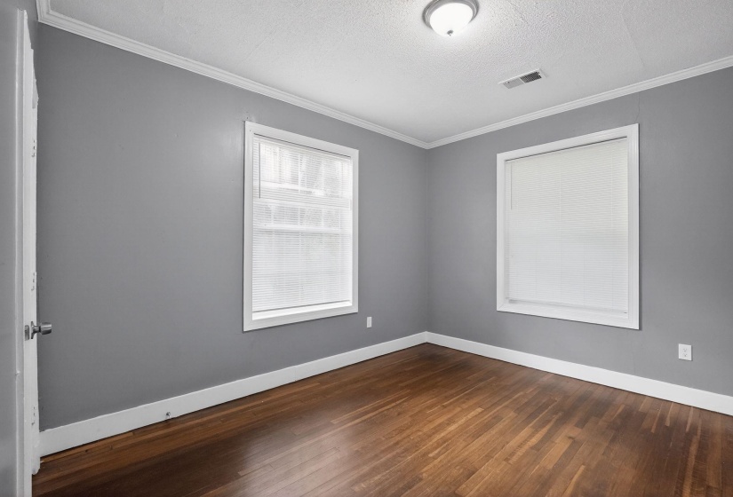 Spacious room featuring wood-finish flooring, two windows, crown molding, and a flush mount ceiling light