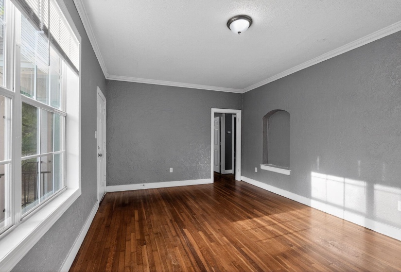 Spacious room featuring rich wood-finish flooring, textured gray walls, and white crown molding