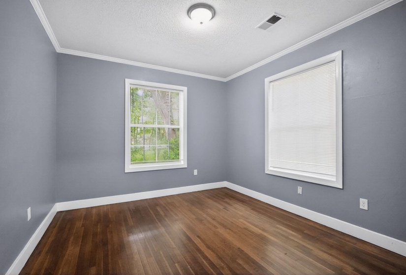 Room featuring wood-finish flooring, two windows with white trim, crown molding, and a flush-mount ceiling light
