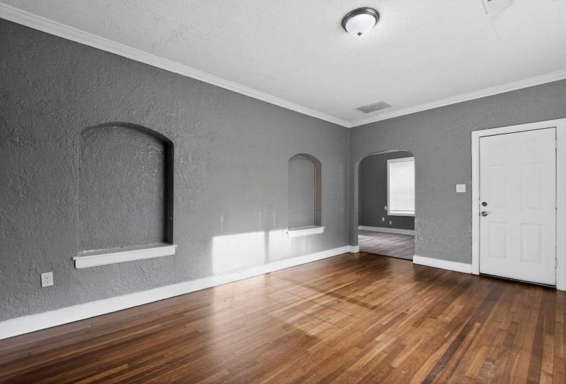 Hardwood flooring throughout featuring arched wall niches, crown molding, and a paneled entry door