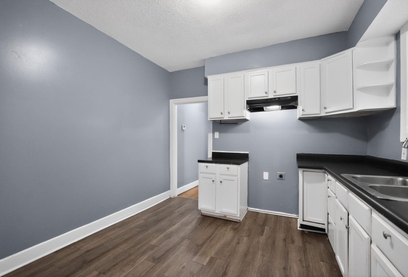 Kitchen featuring white cabinetry with brushed nickel hardware, dark countertops, a double basin stainless steel sink, and wood-finish flooring