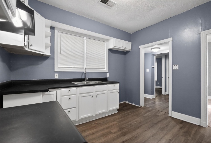 Kitchen featuring wood-finish flooring, white cabinetry, dark countertops, and a stainless steel sink with a single-handle faucet
