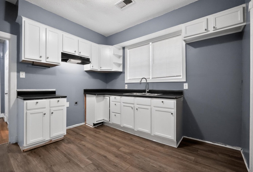 Kitchen featuring wood-finish flooring, white cabinetry, dark countertops, a window with blinds, and a double-basin sink with a gooseneck faucet