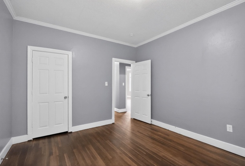 Room featuring wood-finish flooring, light gray walls, white baseboards, and white crown molding