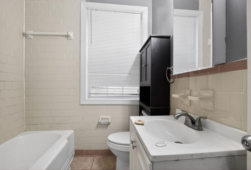 Bathroom featuring a white bathtub, ceramic tile walls, and a window with blinds