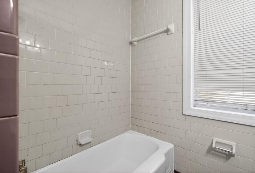 White ceramic tile surround with a white bathtub and window with blinds