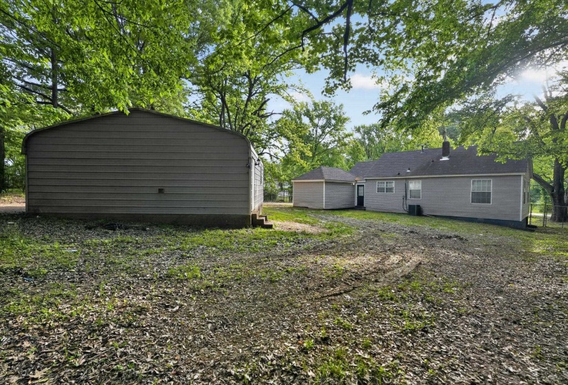 Expansive backyard featuring a detached storage structure and a single-story residence with a grey siding exterior