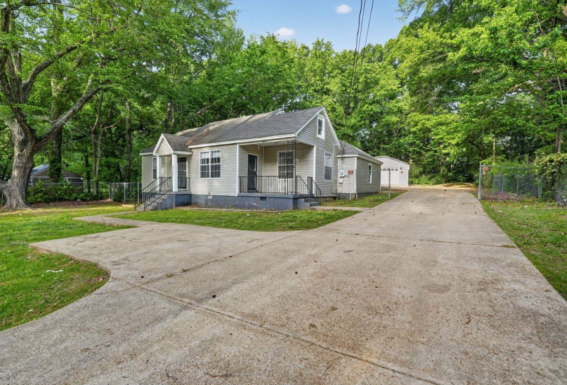 Exterior featuring light-colored siding, a covered entry porch, a long concrete driveway, and mature trees