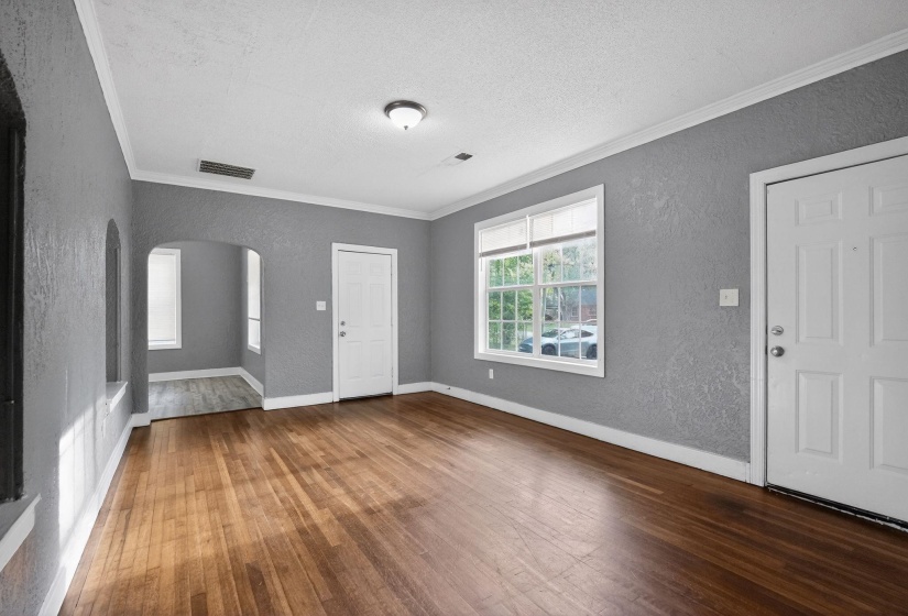 Spacious room featuring wood-finish flooring, textured wall finish, crown molding, a multi-pane window with blinds, and white trim