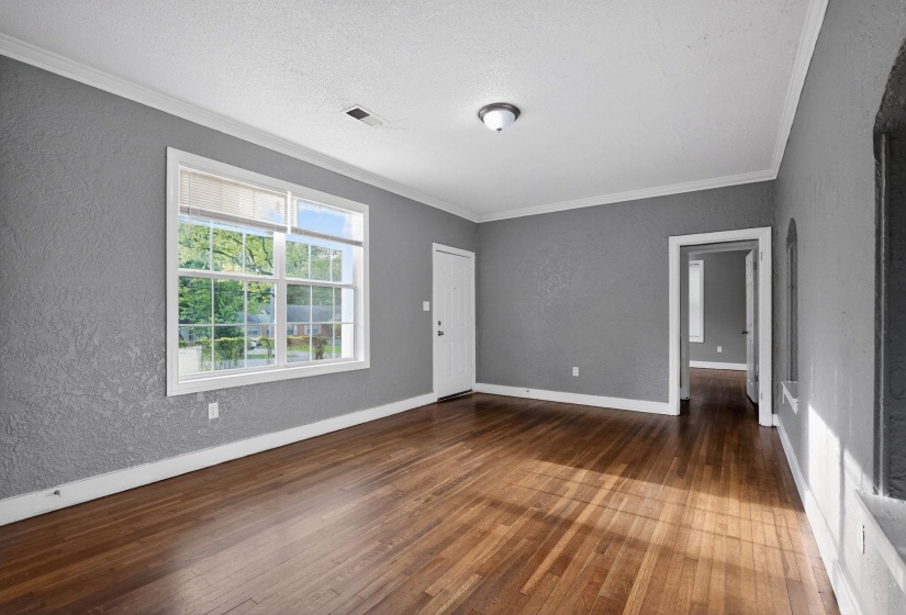 Living area featuring hardwood flooring, grey textured walls, white trim, a large multi-pane window, and a flush-mount ceiling light fixture