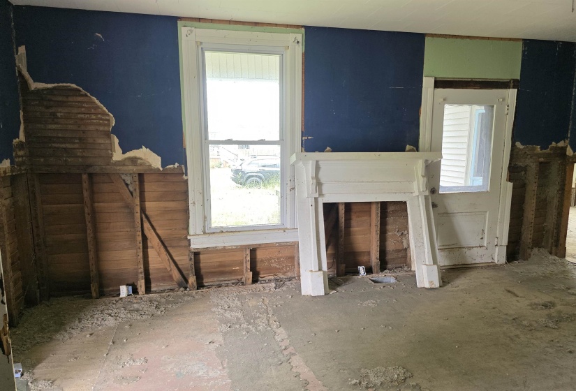 Unfinished interior space featuring exposed lath and plaster, a white mantelpiece, and a single window with white trim