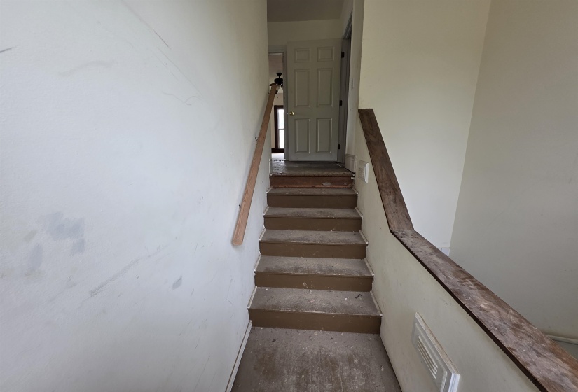 Staircase featuring a wood-finish handrail and light-colored walls