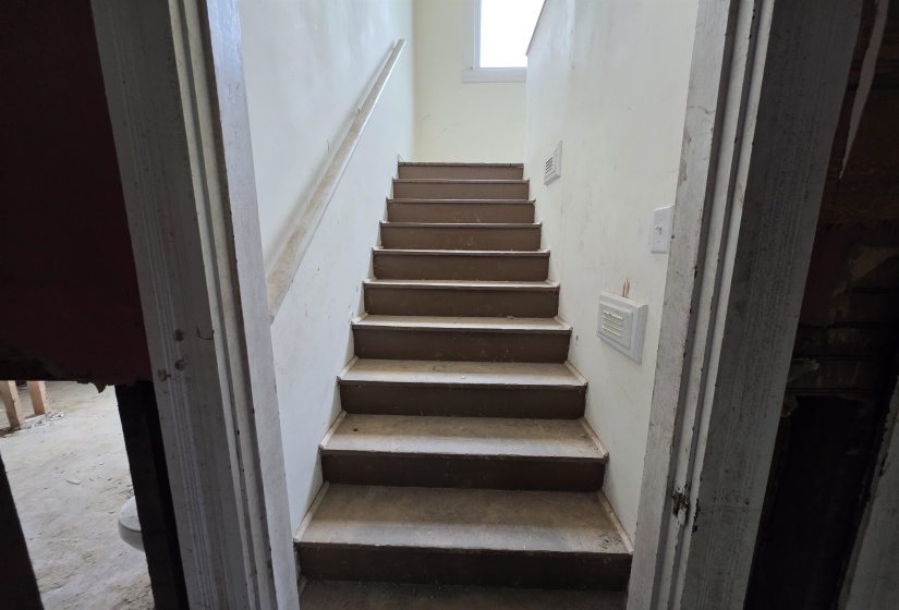 Interior staircase with painted treads and risers, featuring a single handrail and a window at the landing