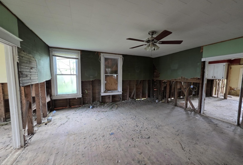 Interior space featuring exposed wall studs, two double-hung windows, and a ceiling fan with integrated lighting