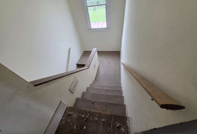 Stairwell featuring a wood-finish handrail, neutral wall tones, and an upper-level window