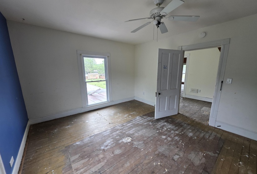 Room featuring a window, wood flooring, a ceiling fan with light fixture, and a solid interior door