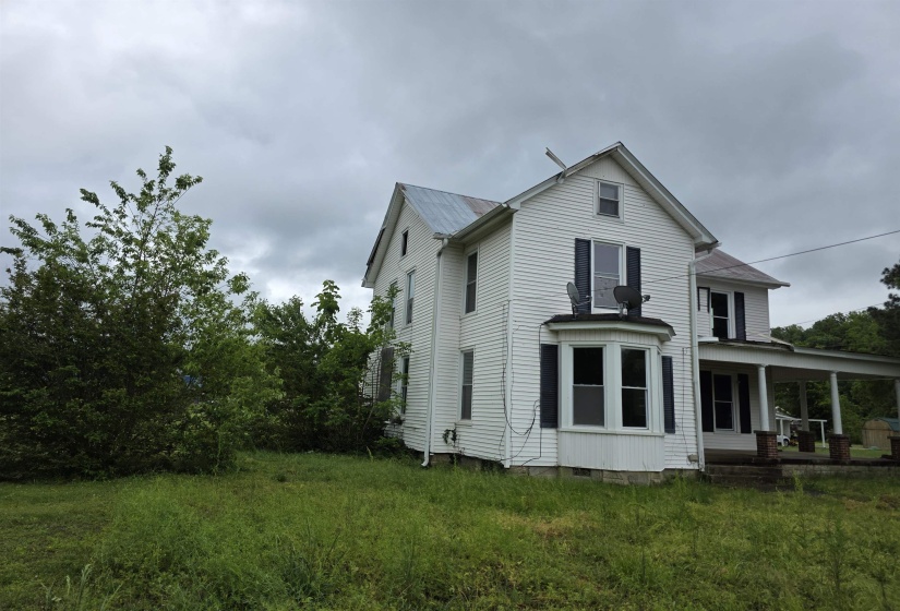 Two-story white siding exterior with a pitched roof, featuring a bay window, dark shutters, and a covered porch