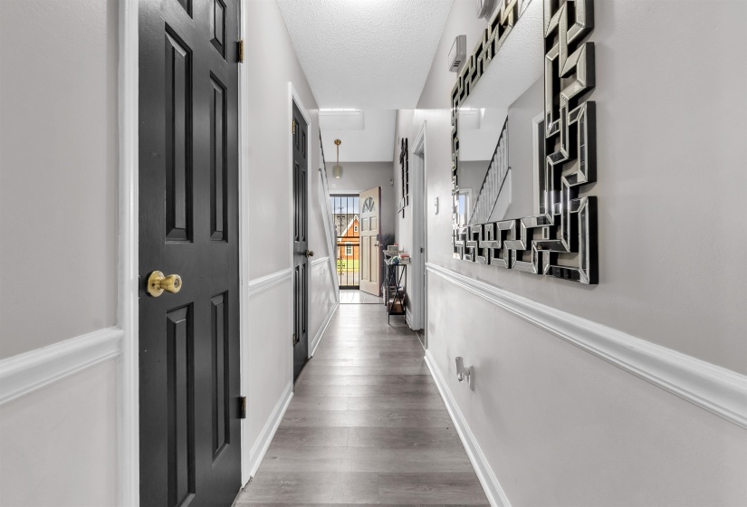 Hallway featuring wood-finish flooring, light gray walls with chair rail molding, and black paneled doors