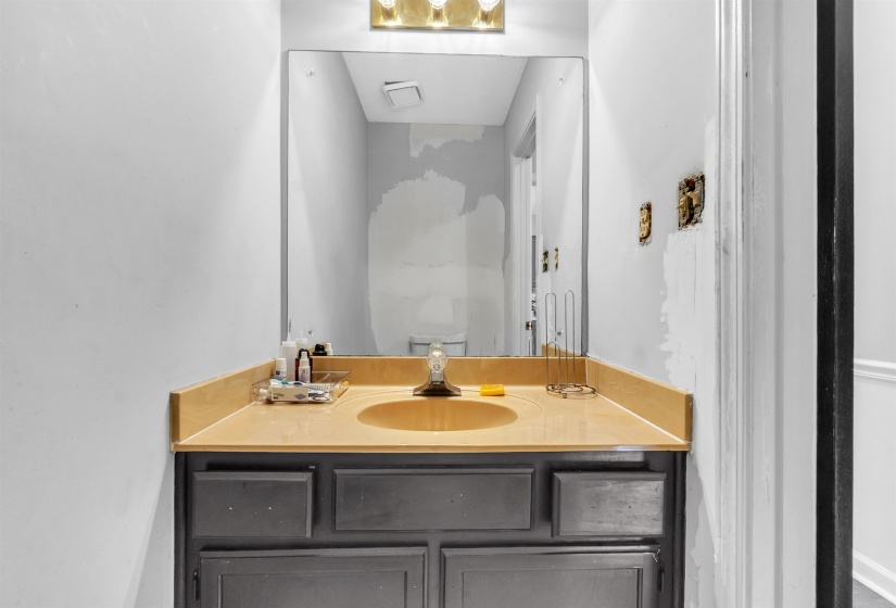 Dark-toned vanity with an integrated sink and light-toned countertop, framed by a wall-mounted mirror and overhead vanity lighting