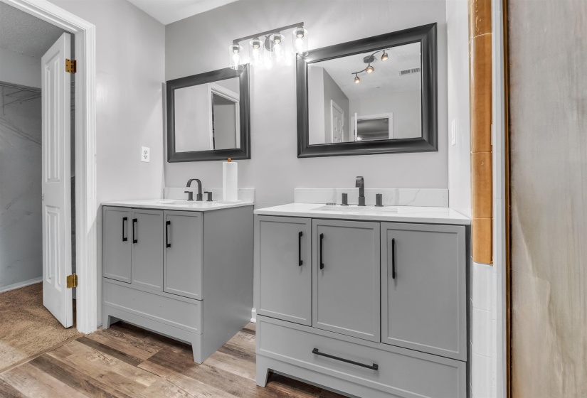 Dual vanity featuring gray cabinetry, white countertops, black hardware, black framed mirrors, and wood-finish flooring