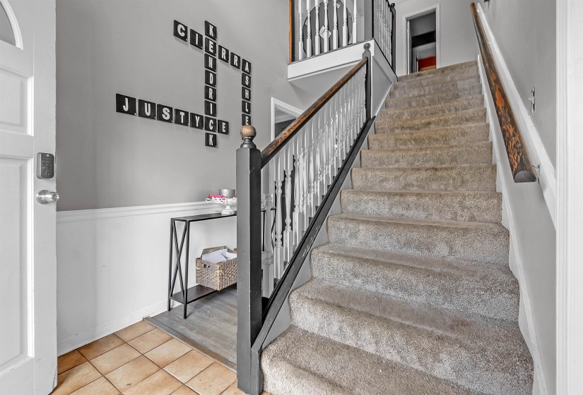 Foyer featuring a multi-level staircase with white balusters and dark newel posts, a wood handrail, and carpeted treads