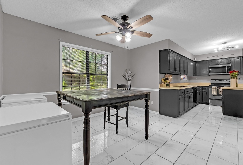 Kitchen featuring a ceiling fan, a large window, dark cabinetry, light countertops, and white tile flooring
