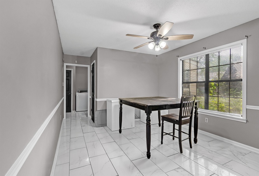 Spacious dining area featuring white tile flooring, a large window with blinds, and a ceiling fan with integrated lighting