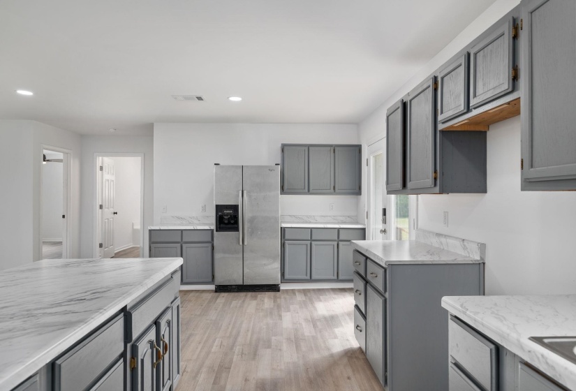 Open-concept kitchen featuring an island, grey cabinetry, stainless steel appliances, marble-look countertops, and wood-finish flooring