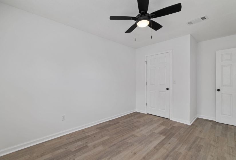 Room featuring wood-finish flooring, white walls, and a black ceiling fan with integrated lighting